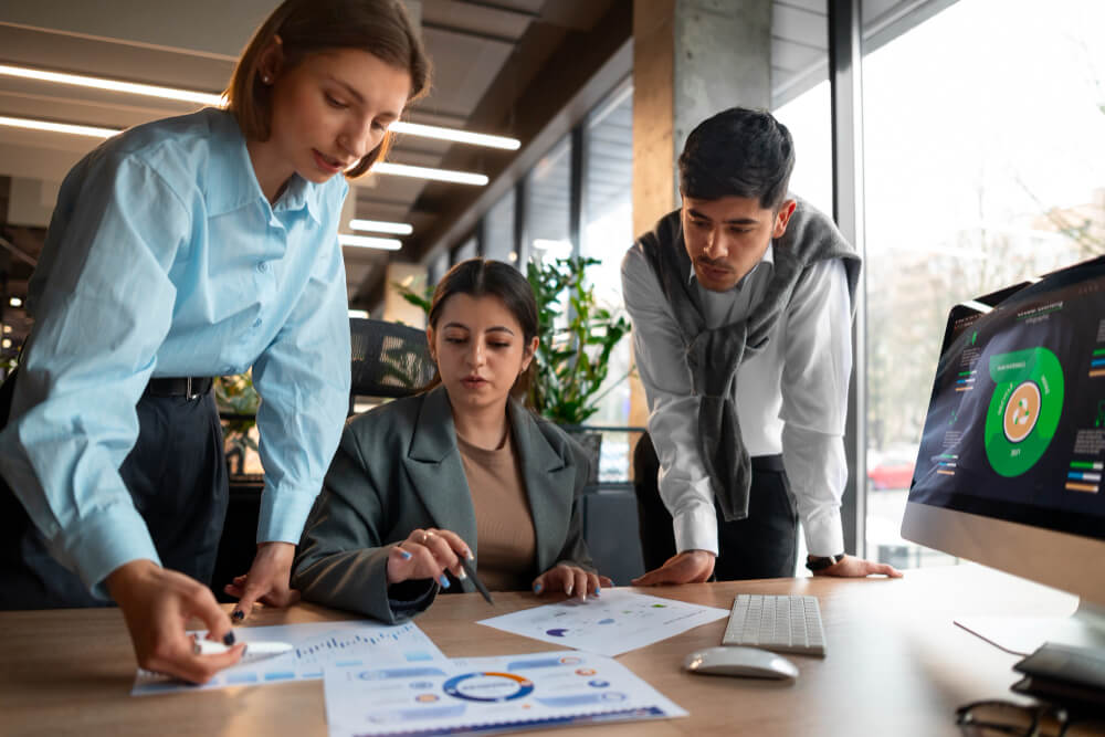 Three colleagues analyzing charts and graphs in a modern office setting.